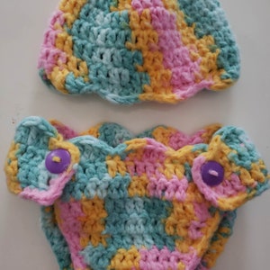 May include: A crocheted baby hat and diaper set in a multi-colored pattern of pink, yellow, and blue.