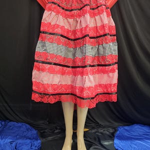 May include: A tiered skirt with a black and white checkered waistband and alternating red and white gingham and black lace panels. Black ribbon accents the red and white sections. The skirt is displayed on a mannequin.