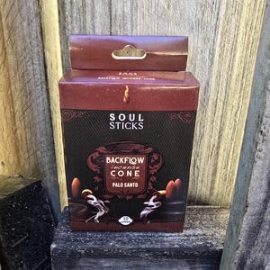 May include: A box of Soul Sticks Backflow Incense Cones in Palo Santo. The box is red and black with a gold design. It features a picture of the cones burning and the smoke flowing upwards. The box says "Soul Sticks Backflow Incense Cone Palo Santo" and "10 cones".