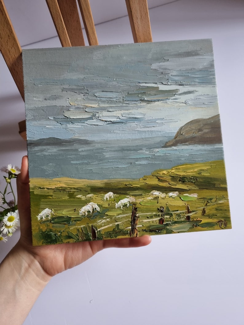 Pode incluir: Pintura a &oacute;leo de uma paisagem com ovelhas pastando num campo verde perto de um corpo de &aacute;gua sob um c&eacute;u nublado. A pintura tem um estilo texturizado, impasto, com pinceladas vis&iacute;veis. A paleta de cores inclui tons de verde, cinza e branco.