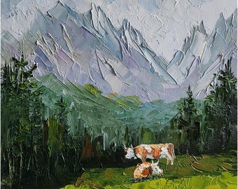 May include: A painting depicting a mountainous landscape with two cows in the foreground. The mountains are painted in shades of blue and purple, with a white cloudy sky. The cows are brown and white, one standing and the other lying down. The foreground is a green field.