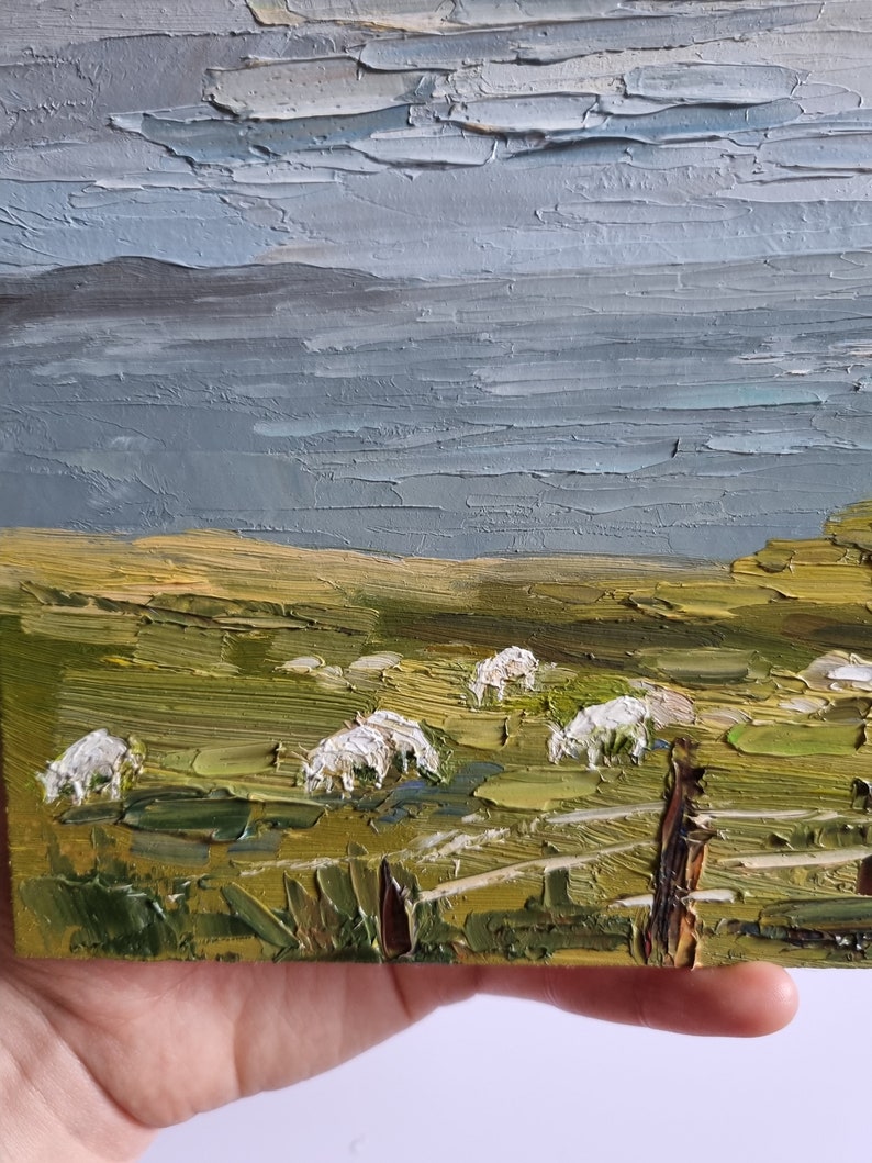 Pode incluir: Pintura a &oacute;leo em impasto de uma paisagem rural com ovelhas pastando num campo verde sob um c&eacute;u nublado. A obra de arte apresenta pinceladas texturizadas e uma paleta de verdes, azuis e amarelos.