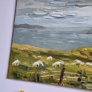 Pode incluir: Pintura a &oacute;leo de uma paisagem costeira com um campo verde, ovelhas brancas e um corpo de &aacute;gua sob um c&eacute;u nublado. Uma cerca de madeira est&aacute; em primeiro plano. A pintura &eacute; em estilo impasto.