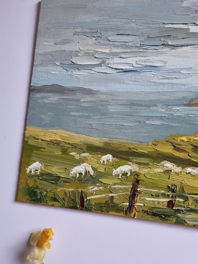 Pode incluir: Pintura a &oacute;leo de uma paisagem costeira com um campo verde, ovelhas brancas e um corpo de &aacute;gua sob um c&eacute;u nublado. Uma cerca de madeira est&aacute; em primeiro plano. A pintura &eacute; em estilo impasto.