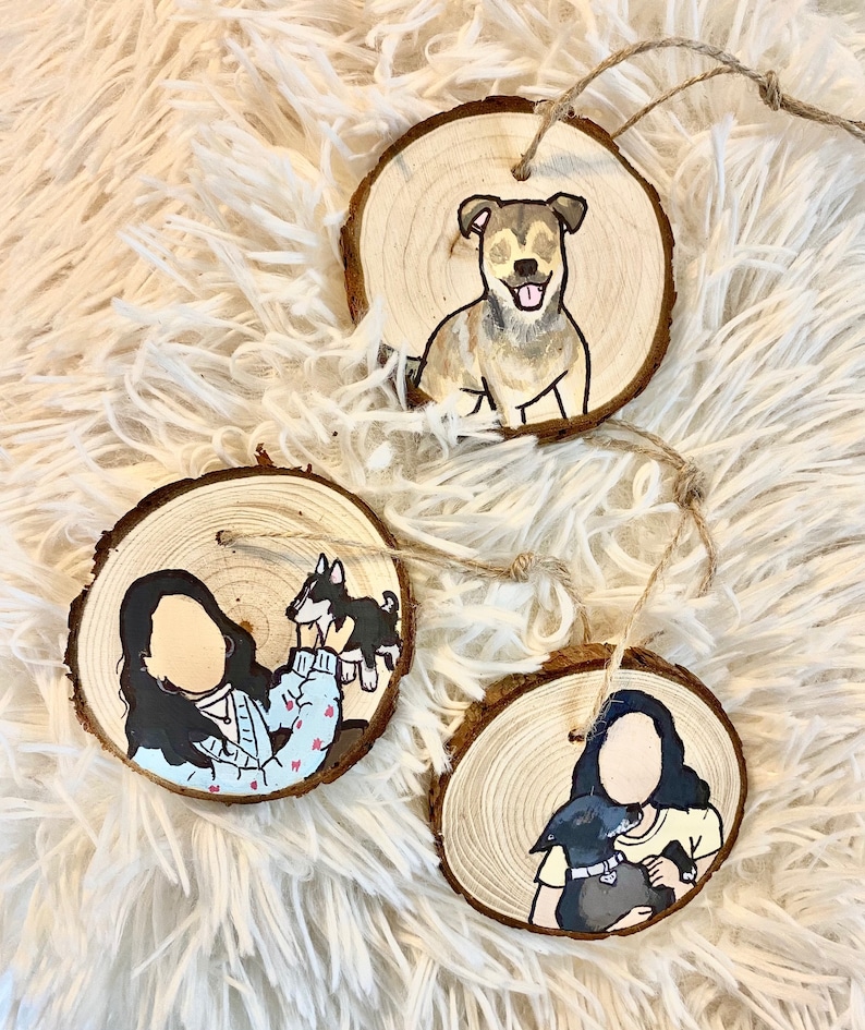 May include: Three round wooden ornaments with painted portraits of people and their pets. The first ornament features a brown and white dog. The second ornament features a person holding a small black and white dog. The third ornament features a person holding a black dog.
