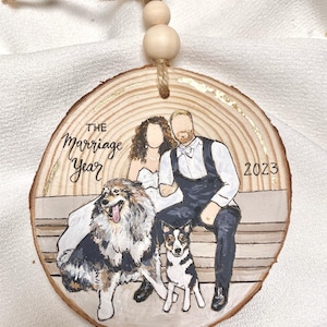 May include: A round wooden ornament with a gold accent, featuring a painted portrait of a couple and two dogs. The text "THE marriage Year 2023" is written on the ornament.