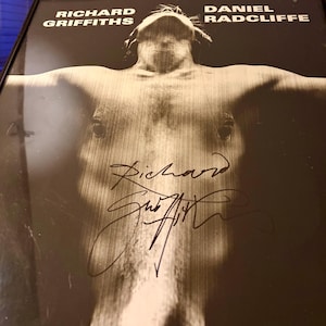 May include: Black and white framed photograph featuring Richard Griffiths and Daniel Radcliffe. The image shows a shirtless person with outstretched arms, with signatures in the lower portion. The names Richard Griffiths and Daniel Radcliffe are printed at the top.