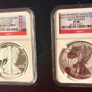 May include: Two silver coins in protective cases. The coins are from the 2012 S Eagle set, with the text "San Francisco Eagle Set" and "First Releases" visible. The coins feature a walking Liberty design and are graded PF 70.