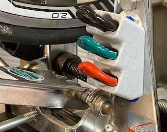May include: A silver bicycle tire repair stand with a black base and a lever. The stand has a tire mounted on it and a tool holder with three tire levers. The tool holder is white with blue, green, and red tire levers.