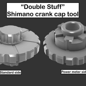 May include: Two grey "Double Stuff" Shimano crank cap tools are shown. The standard side has a central knob with radial grooves and a toothed outer edge. The power meter side has a central opening and a toothed outer edge.