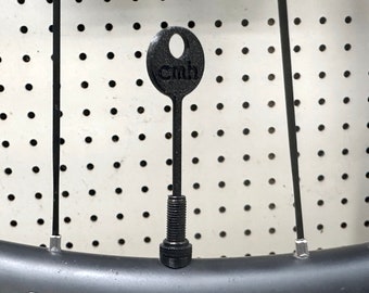 May include: A black bicycle valve stem with a black plastic cap that says "cmh" on it.