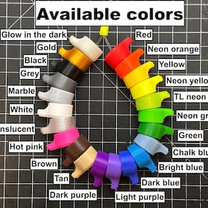 May include: A variety of colorful, 3D-printed objects are arranged in a circular pattern. The image displays a range of colors, including red, yellow, green, blue, and purple, as well as neutral tones like black, white, and grey. Text at the top reads "Available colors."