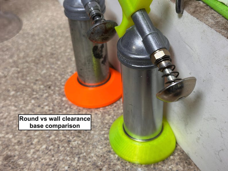 May include: Two metal cylindrical tools with silver bodies and spring-loaded nozzles. One tool has an orange base, the other a neon green base. Text in the image reads "Round vs wall clearance base comparison."