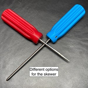 Può includere: Due diverse opzioni per uno spiedino, uno con manico rosso e uno con manico blu. Entrambi gli spiedini hanno un'asta di metallo.