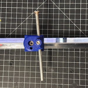 May include: A blue and silver glass cutter with a metal rod extending from the blue handle. The cutter is on a black grid surface.