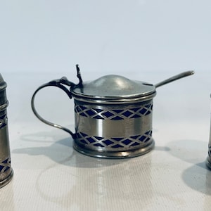 May include: A set of three silver salt and pepper shakers with blue glass accents. The shakers feature a decorative design and are in excellent condition.