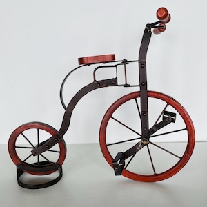 Könnte beinhalten: Ein dekoratives Metall-Dreirad mit Holzrädern und einem Holzsitz. Das Dreirad ist schwarz lackiert mit roten Akzenten.