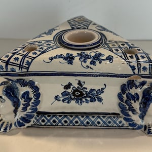 May include: A triangular ceramic inkwell with blue and white floral designs. The inkwell has three wells and sits on three lion's head feet.
