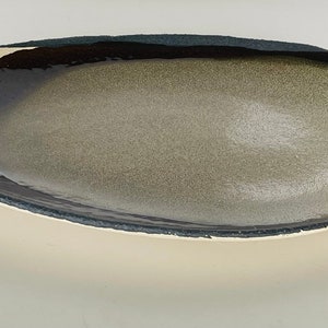 May include: A large, oval ceramic serving platter with a dark brown glaze that fades to a light grey. The platter has a slightly irregular edge.