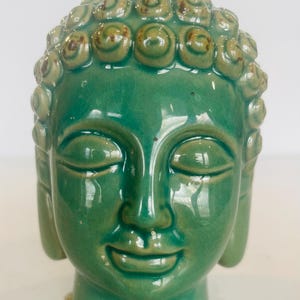 May include: A green ceramic Buddha head sculpture with a serene expression and a detailed headpiece.