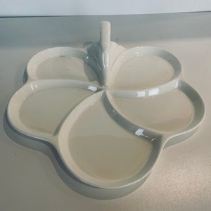 Könnte beinhalten: Weiße Keramik-Servierplatte mit fünf Abschnitten und einem Griff. Die Platte ist blumenförmig.