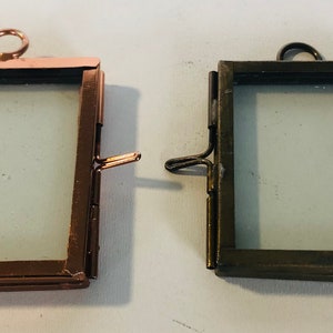 May include: Two small, empty picture frames with glass fronts. The frame on the left is copper coloured and the frame on the right is a darker bronze colour.