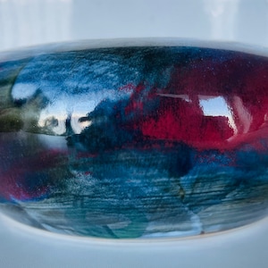 May include: A ceramic bowl with a deep red, blue, and green glaze. The bowl has an organic, abstract design.