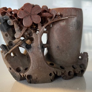 May include: A carved stone sculpture of a tree with a flower on top and a small vase. The sculpture is made of brown and black stone and has a detailed design.