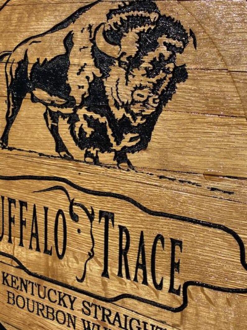 以下が含まれることがあります： 黒いバッファローのイラストと、曲がったバナーに「BUFFALO TRACE」という文字が描かれた木製の看板。看板には、ケンタッキー・ストレート・バーボン・ウイスキーに関するテキストも含まれています。