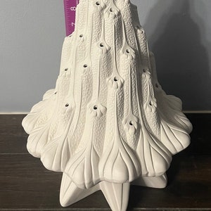 Può includere: Albero di Natale in ceramica bianca con una cima a forma di stella e una superficie testurizzata. L'albero ha una base a forma di stella ed è decorato con fori per le luci.