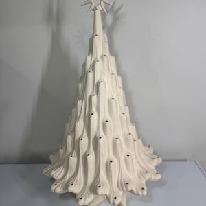 Puede incluir: Una escultura de árbol de Navidad de cerámica en color blanco roto mate con un diseño de ramas texturizadas y fluidas que presenta numerosas aberturas circulares pequeñas para luces. El árbol está rematado con una punta en forma de estrella.