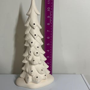 May include: A white ceramic Christmas tree with a textured surface and small holes for lights. The tree is approximately 30 cm tall and sits on a rounded base. A purple ruler is next to the tree.