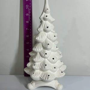 May include: A white ceramic Christmas tree with a textured, layered design. The tree has small holes for lights and sits on a decorative base. The tree is approximately 30 cm tall.