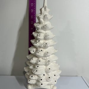 Könnte beinhalten: Ein weißer Weihnachtsbaum aus Keramik mit strukturierter Oberfläche. Der Baum hat mehrere Schichten mit kleinen Löchern und eine spitze Spitze. Der Baum ist etwa 38 cm hoch.
