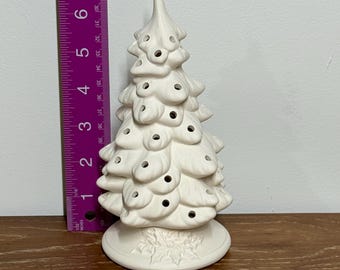 May include: A white ceramic Christmas tree with a textured surface and round openings. The tree is approximately 6 inches tall and sits on a round base with a holly leaf design. The tree is unpainted.