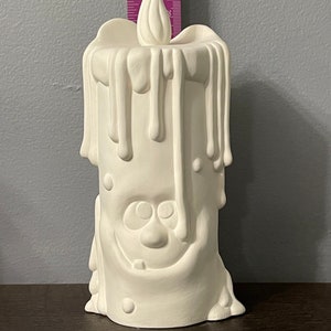 Könnte beinhalten: Weiße Kerze aus Keramik mit einem tropfenden Wachsdesign und einem lächelnden Gesicht. Die Kerze ist etwa 15 cm hoch.