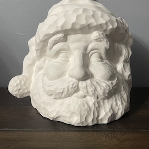 May include: White ceramic Santa Claus head with a detailed, textured beard and hat. The Santa Claus is smiling with his eyes closed.