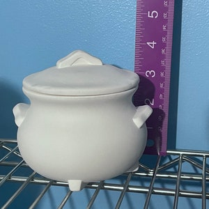 Peut inclure: Chaudron en céramique blanche avec un couvercle, doté d'un corps arrondi et de trois petits pieds. Le chaudron mesure environ 10 cm de haut.