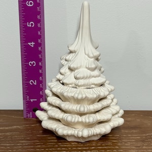 以下が含まれることがあります： クリーム色のセラミッククリスマスツリー。テクスチャード加工されたレイヤーデザイン。高さ約15cm。木製の表面に置かれています。定規が木の隣にあります。