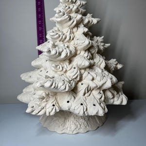 Può includere: Un albero di Natale in ceramica di colore bianco sporco. L'albero ha un design strutturato e dettagliato con più strati di rami e piccoli fori per le luci. L'albero è alto circa 40 cm.