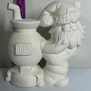 May include: A white ceramic Santa Claus figurine holding onto a white stove. The Santa figure has a hat with a fur trim and a long beard. The stove has a door and a chimney. The figurine is unpainted and ready for customization.