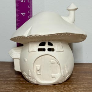 以下が含まれることがあります： 未塗装のセラミック製キノコハウス。煙突、ドア、窓が付いています。高さは約13cmで、キノコの傘の屋根が付いています。ドアには小さな取っ手があり、窓にはカーテンが付いています。塗装して装飾する準備ができています。