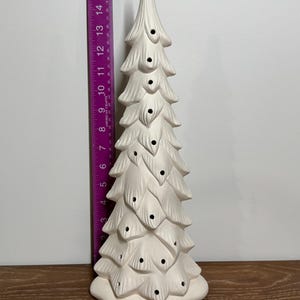 May include: A white ceramic Christmas tree with a textured, layered design. The tree has several cut-out holes and is approximately 10 inches tall. The tree is unpainted and ready for customization.