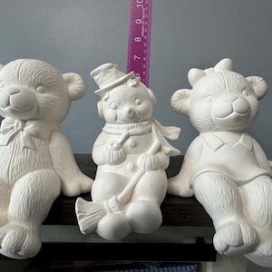 Puede incluir: Tres figuras de cerámica blanca: un oso con un lazo, un muñeco de nieve con una escoba y un oso con un collar. Las figuras están listas para ser pintadas.