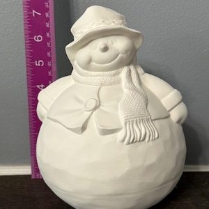 以下が含まれることがあります： 黒い帽子、白いマフラー、黒いボタンのついた白いセラミック製の雪だるまの置物です。