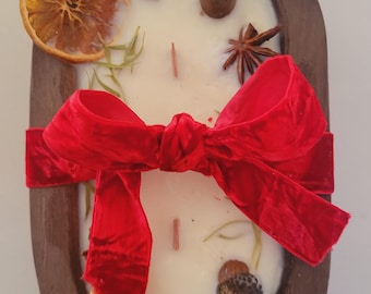 May include: A white candle in a wooden bowl with a red velvet bow, cinnamon sticks, dried orange slices, pine cones, and acorns.