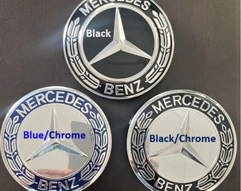 May include: Three Mercedes-Benz emblems with different color combinations. The first emblem has a black star on a black background. The second emblem has a silver star on a silver background with a blue outer ring. The third emblem has a silver star on a silver background with a black outer ring.
