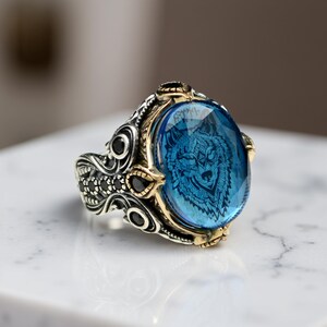 May include: A silver ring with a blue stone featuring a wolf design. The ring is decorated with black stones and intricate details.