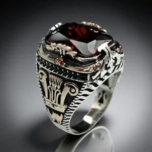 May include: A silver ring featuring a large, dark red gemstone with multiple facets. The ring has detailed carvings and small accent stones. The design incorporates Egyptian-inspired motifs, creating a bold and striking appearance.
