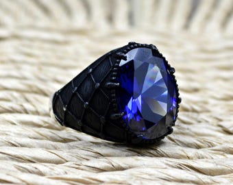 Puede incluir: Un anillo negro con una gran piedra preciosa azul oscuro facetada. La banda del anillo tiene un diseño texturizado y estampado.